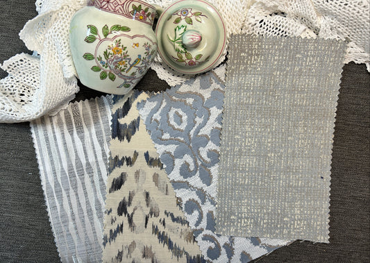 A flat-lay display of various fabric and textile swatches, including striped lace, floral ikat, and textured linen, alongside two vintage floral ceramic lidded boxes on a gray textured background.